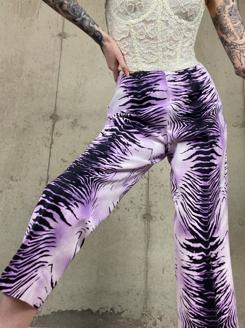 May include: Purple and black zebra print pants. The pants have a wide leg and a high waist.