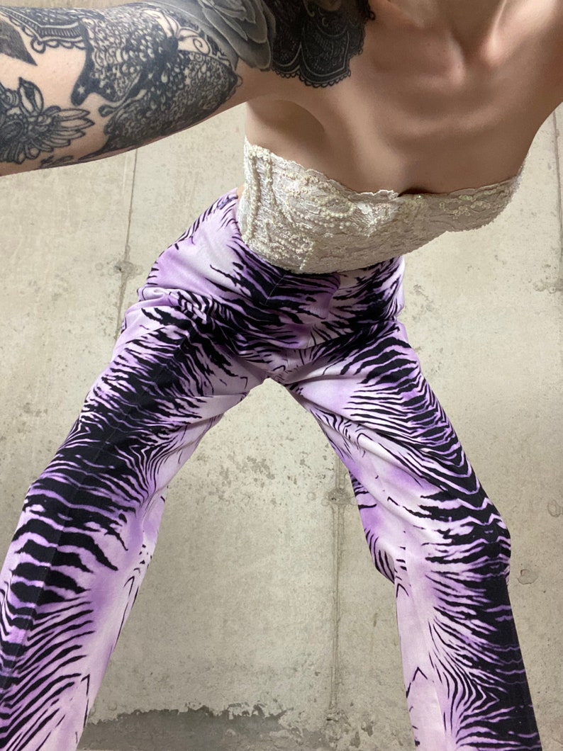May include: A person wearing a white lace strapless top and purple and black zebra print pants.