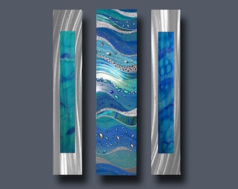 May include: Three vertical metal wall art panels with a blue and silver abstract design. The panels feature a wavy pattern with blue and silver accents.