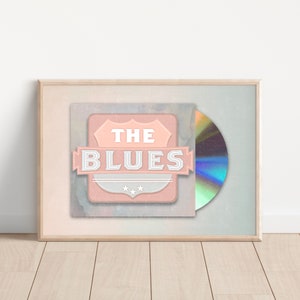 Puede incluir: Un CD enmarcado con un diseño rosa y blanco con el texto "THE BLUES" en estilo vintage. El CD está en una caja de plástico transparente.