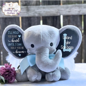 May include: A gray plush elephant with blue wings and a black felt ear with the text "I'll hold you in my heart until I can hold you in heaven" and "Leland Tyler Santiago".