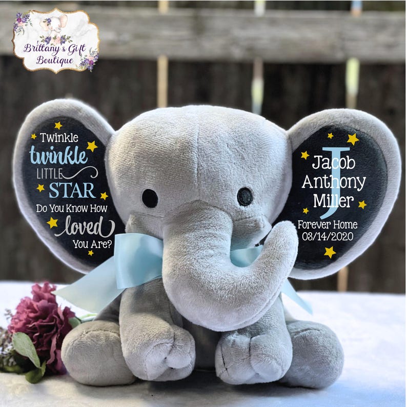 May include: A gray plush elephant toy with a light blue ribbon tied around its neck. The left ear features the text Twinkle twinkle LITTLE STAR Do You Know How loved You Are? and the right ear displays the name Jacob Anthony Miller.