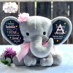 May include: A plush gray elephant toy with a pink ribbon and flower, featuring black ears printed with yellow stars and text: Twinkle twinkle LITTLE STAR Do You Know How loved YOU ARE? and Aubrey Maria Miller Forever Home 03/14/2020.