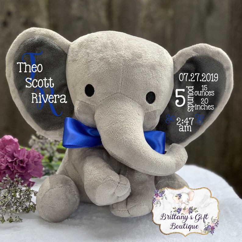 May include: A gray plush elephant with a blue bow tie. The elephant's ears display the name "Theo Scott Rivera" and birth details: 5 pounds, 15 ounces, 20 inches, and the time and date of birth.