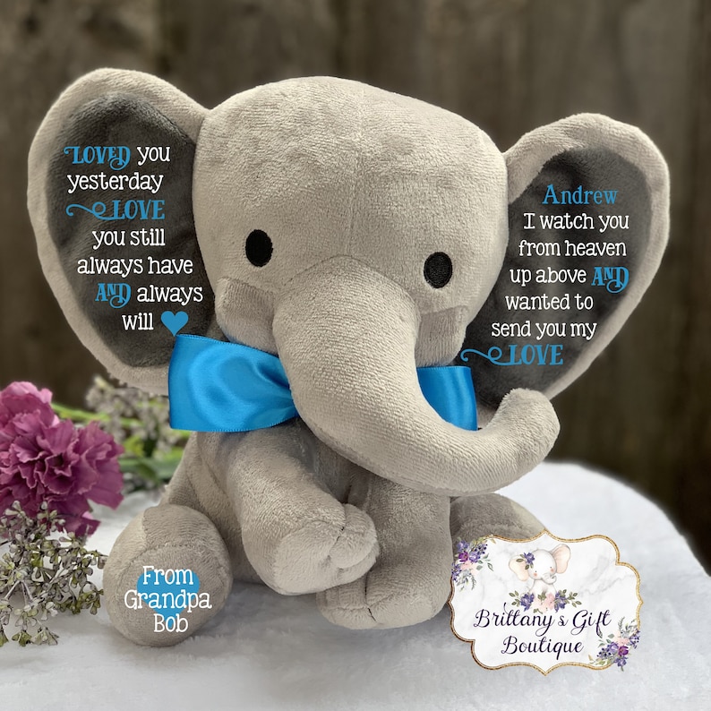 Puede incluir: Un elefante de peluche gris con una pajarita azul. El elefante tiene texto bordado que dice "Loved you yesterday, Love you still, always have and always will." y "Andrew, I watch you from heaven up above and wanted to send you my love." El elefante est&aacute; sentado sobre una superficie blanca con una etiqueta que dice "From Grandpa Bob" y "Brittany's Gift Boutique".