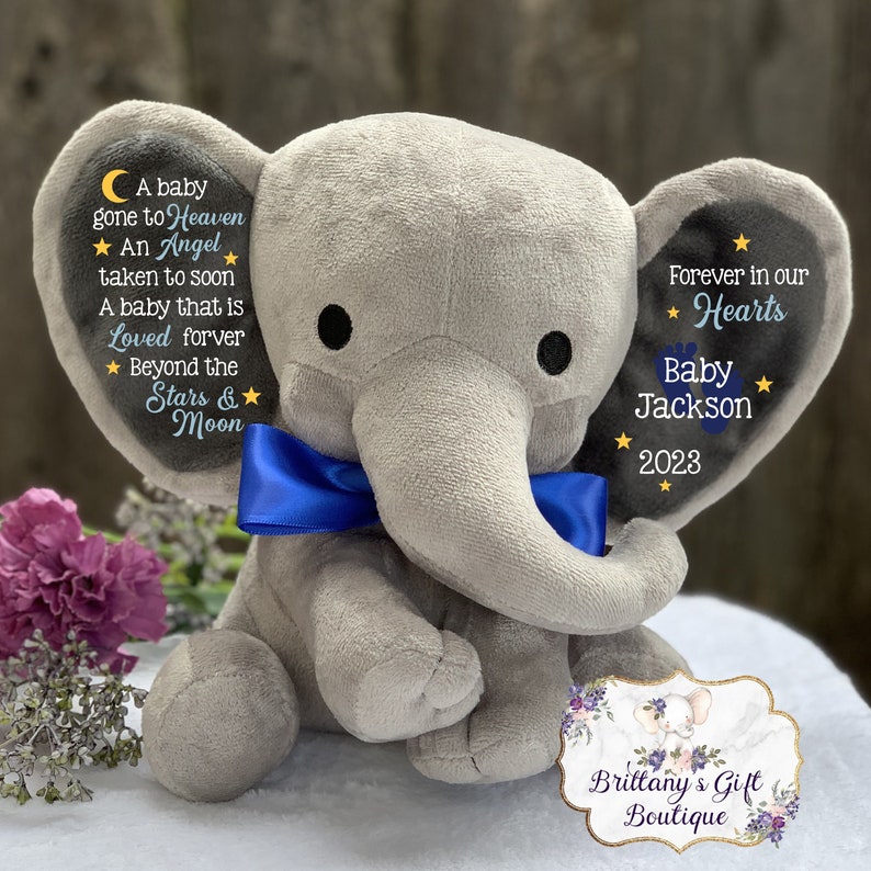 Puede incluir: Un elefante de peluche gris con una pajarita azul. El elefante tiene texto bordado en sus orejas, incluyendo "A baby gone to Heaven, An Angel taken to soon, A baby that is Loved forever, Beyond the Stars & Moon" y "Forever in our Hearts, Baby Jackson, 2023".