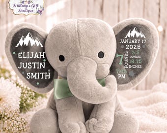 May include: A plush gray elephant toy with a light green satin bow tie. The elephant's ears feature white printed text and graphics, including the name Elijah Justin Smith, the date January 17 2025, and birth stats of 7 pounds 3.5 ounces and 19.75 inches.