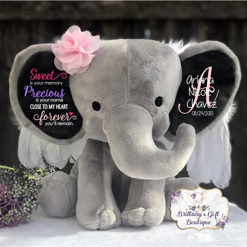 May include: A gray plush elephant with black ears and a pink flower on its head. Text on the elephant includes the name "Ariana Nicole Chavez" and the date "08/24/2013". Additional text reads "Sweet is your memory, Precious is your name, Close to my heart forever you'll remain."