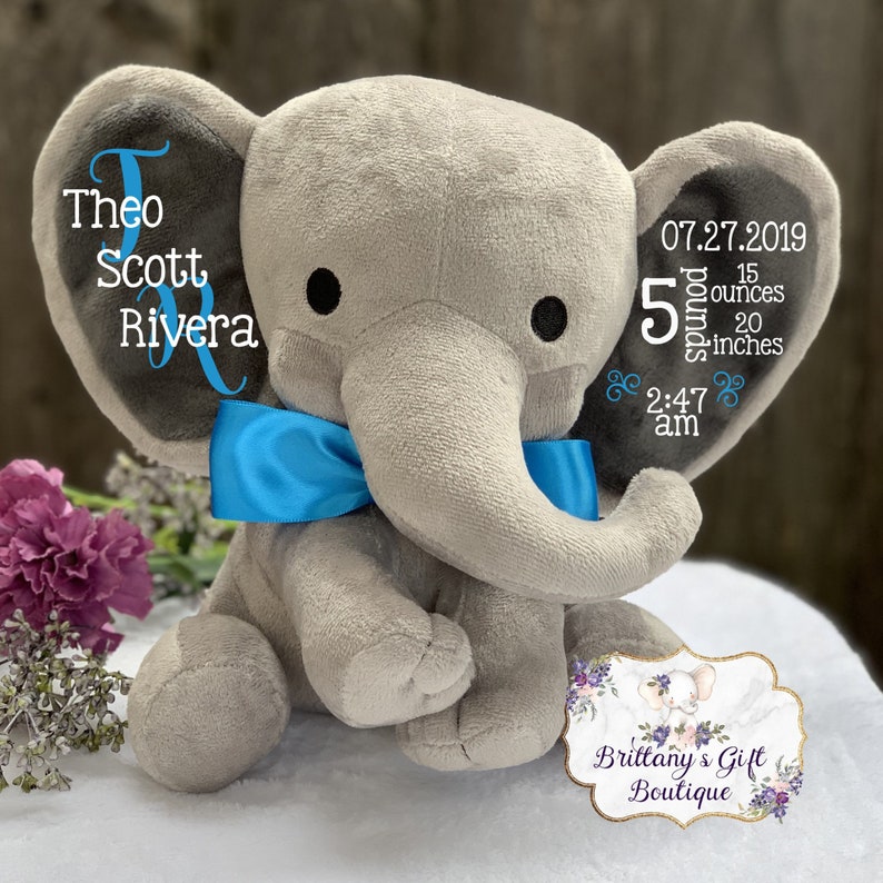 May include: A gray plush elephant with a blue bow tie. The elephant's ear displays the name "Theo Scott Rivera" and birth details: 5 pounds, 15 ounces, 20 inches, and the date and time of birth.