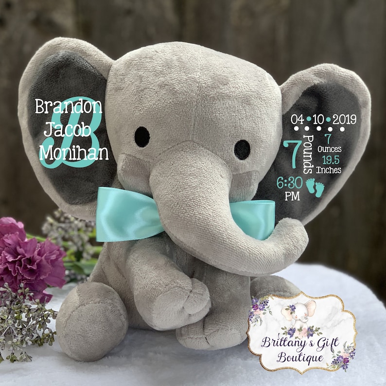 May include: A plush gray elephant toy with a light blue satin bow around its neck. The left ear features the text Brandon Jacob Monihan. The right ear displays the date 04-10-2019, 7 Pounds 7 Ounces, 19.5 Inches, 6:30 PM, and two footprint icons.