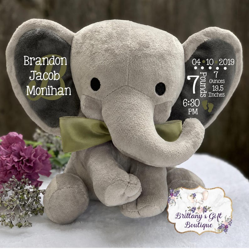 May include: A plush gray elephant toy with a green ribbon around its neck. The left ear features the name Brandon Jacob Monihan. The right ear displays the birth date 04-10-2019, 7 Pounds 7 Ounces, 19.5 Inches, and 6:30 PM with two small footprint icons.