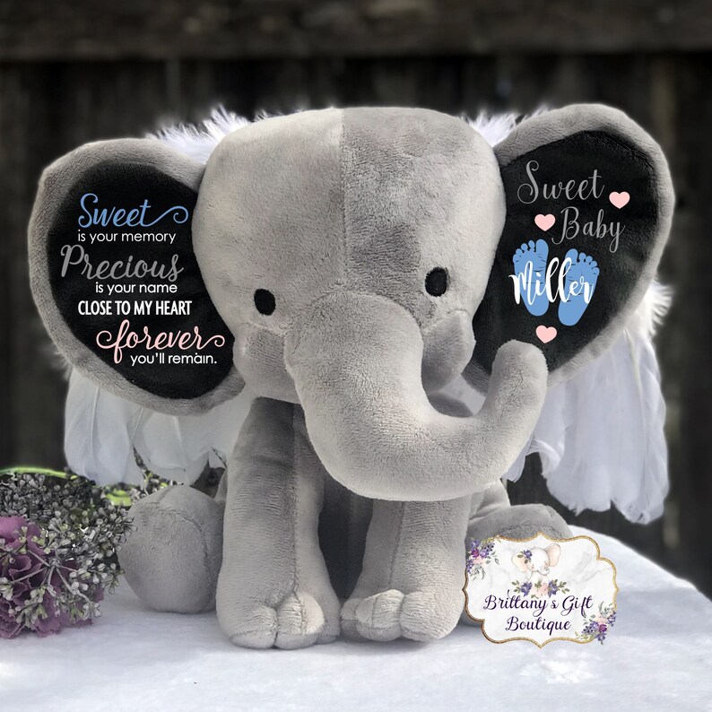 May include: A gray plush elephant with white accents and black eyes. The elephant's ears have text that reads "Sweet Baby Miller" and "Sweet is your memory Precious is your name Close to my heart forever you'll remain." A small tag reads "Brittany's Gift Boutique."