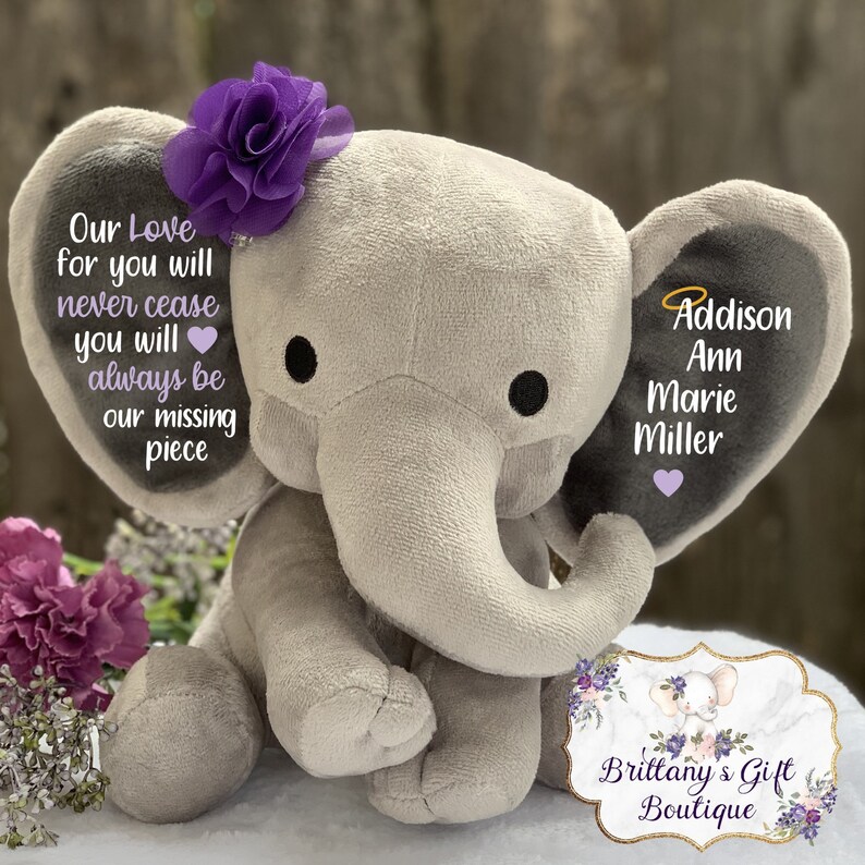 Może przedstawiać: Szary pluszowy słoń z fioletowym kwiatem na głowie. Słoń ma na jednym uchu napis "Our Love for you will never cease you will always be our missing piece". Na drugim uchu widnieje imię "Addison Ann Marie Miller". Słoń siedzi na białym tle.