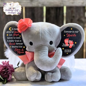 Puede incluir: Un elefante de peluche gris con una cinta rosa y una flor en la cabeza. Las orejas del elefante tienen parches de fieltro negro con el texto "A baby gone to Heaven, An Angel taken to soon, A baby that is Loved forever, Beyond the Stars & Moon" y "Forever in our Hearts, Baby Jackson, 2023".
