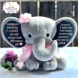 Puede incluir: Un elefante de peluche gris con orejas rosas y un lazo rosa. El elefante tiene mensajes bordados en sus orejas que dicen "Loved you yesterday Love you still always have and always will" y "Annabella I watch you from heaven up above and wanted to send you my Love". El elefante tambi&eacute;n tiene una flor rosa en la cabeza y las palabras "From Grandpa Bob" en su pie.