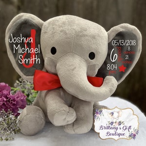 K&ouml;nnte beinhalten: Ein graues Pl&uuml;schelefant-Spielzeug mit einer roten Satinschleife um den Hals. Das linke Ohr zeigt den Text Joshua Michael Smith mit einem roten J. Das rechte Ohr zeigt 05/13/2018, 6 pounds 8 ounces, 21 inches, 8:04 pm und einen roten Stern.