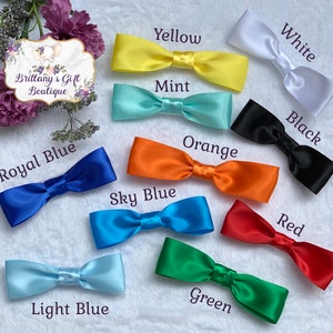 Op de afbeelding: Assortiment van tien satijnen strikken in verschillende kleuren, waaronder geel, wit, mint, zwart, oranje, hemelsblauw, lichtblauw, groen en rood. De strikken zijn in een cirkel op een wit oppervlak gerangschikt.