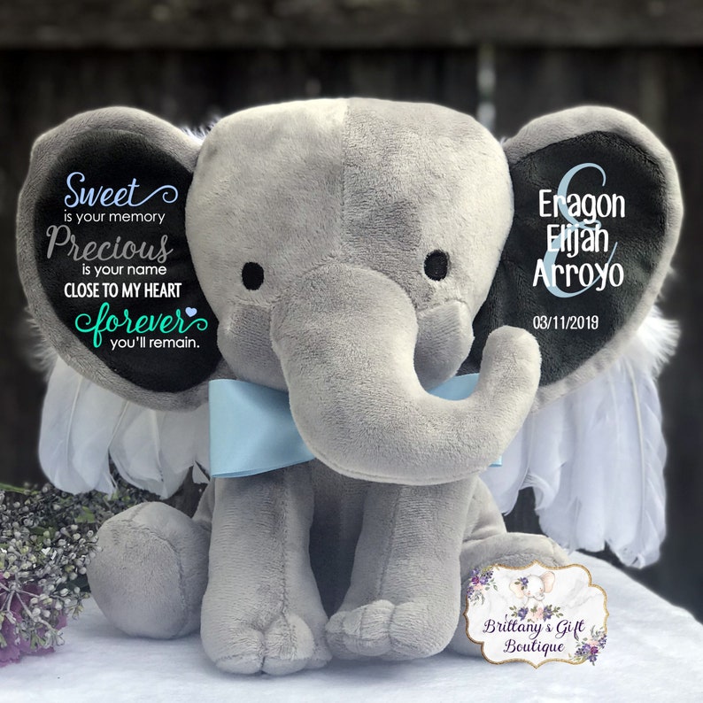 May include: A gray plush elephant with a light blue bow tie. The elephant's ears have text that reads "Sweet is your memory, Precious is your name, CLOSE TO MY HEART forever you'll remain." The other ear has the name "Eragon Elijah Arroyo" and the date "03/11/2019".