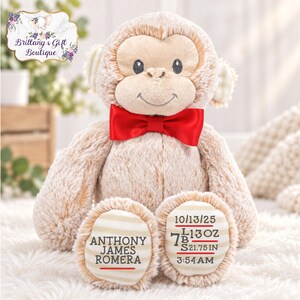 May include: A plush tan monkey toy featuring a bright red satin bow tie around its neck. The monkey has striped fabric on its ears and feet. The left foot displays the name Anthony James Romera, and the right foot shows 10/13/25, 7 lbs 13 oz, 21.75 in, 3:54 AM.