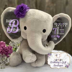 May include: A plush gray elephant toy with a purple fabric flower on its head. The left ear displays the name Bailey Jane Monihan. The right ear features the date 04-10-2019, 7 Pounds 7 Ounces, 19.5 Inches, and 6:30 PM with two small footprint icons.