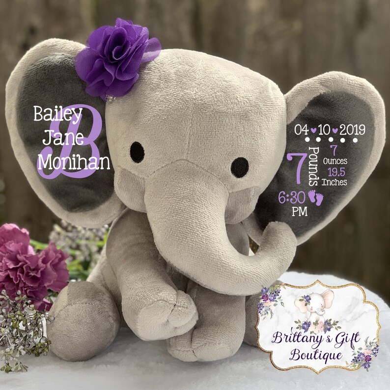 May include: A plush gray elephant toy with a purple fabric flower on its head. The left ear displays the name Bailey Jane Monihan. The right ear features the date 04-10-2019, 7 Pounds 7 Ounces, 19.5 Inches, and 6:30 PM with two small footprint icons.