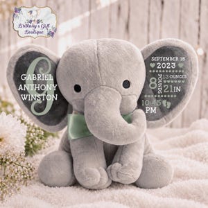 May include: A gray plush elephant toy with a sage green satin bow tie. The left ear features the name Gabriel Anthony Winston. The right ear displays birth details: September 18, 2023, 8 pounds 13 ounces, 21 inches, and 10:45 PM with footprints.