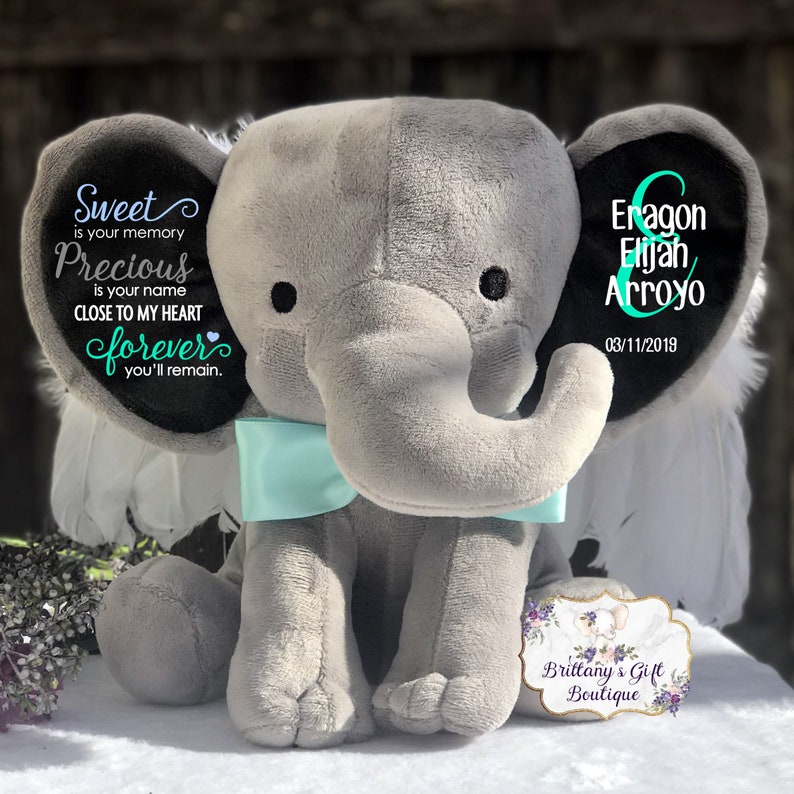 May include: A gray plush elephant with a light blue bow tie. The elephant's ears have text that reads "Sweet is your memory, Precious is your name, Close to my heart forever you'll remain." The other ear has the name "Eragon Elijah Arroyo" and the date "03/11/2019."