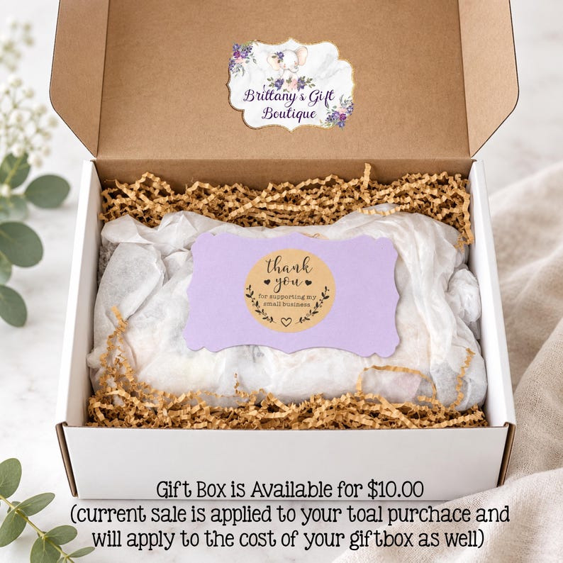 May include: A white cardboard gift box filled with brown crinkle paper and white tissue paper. A label inside the lid reads Brittany's Gift Boutique. A light purple card with a circular sticker reading thank you for supporting my small business.