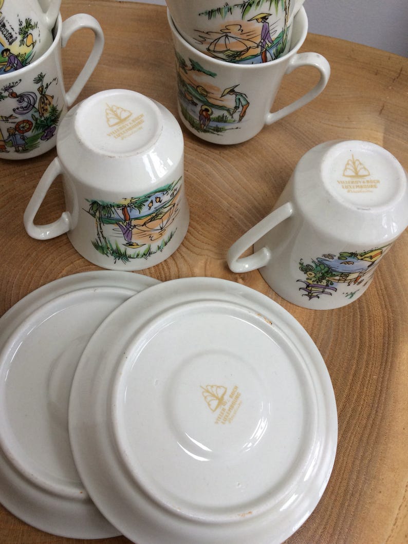 May include: Set of four white ceramic teacups with colorful illustrations of people fishing and sailing. The cups have gold lettering on the bottom that reads "Valenciennes & Sons, Ltd. England". The set also includes two white ceramic saucers with the same gold lettering on the bottom.