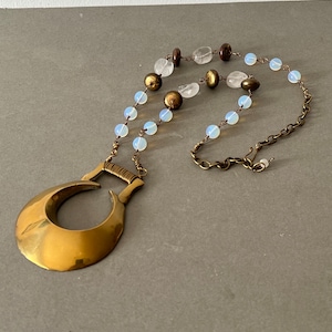 Könnte beinhalten: Eine goldene Halskette mit einem Halbmond-Anhänger, einer Kette und einer Perlenkette mit weißen und braunen Perlen.