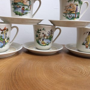 May include: Set of six white teacups and saucers with colorful Asian-inspired designs. Each cup features a different scene with people, buildings, and nature.