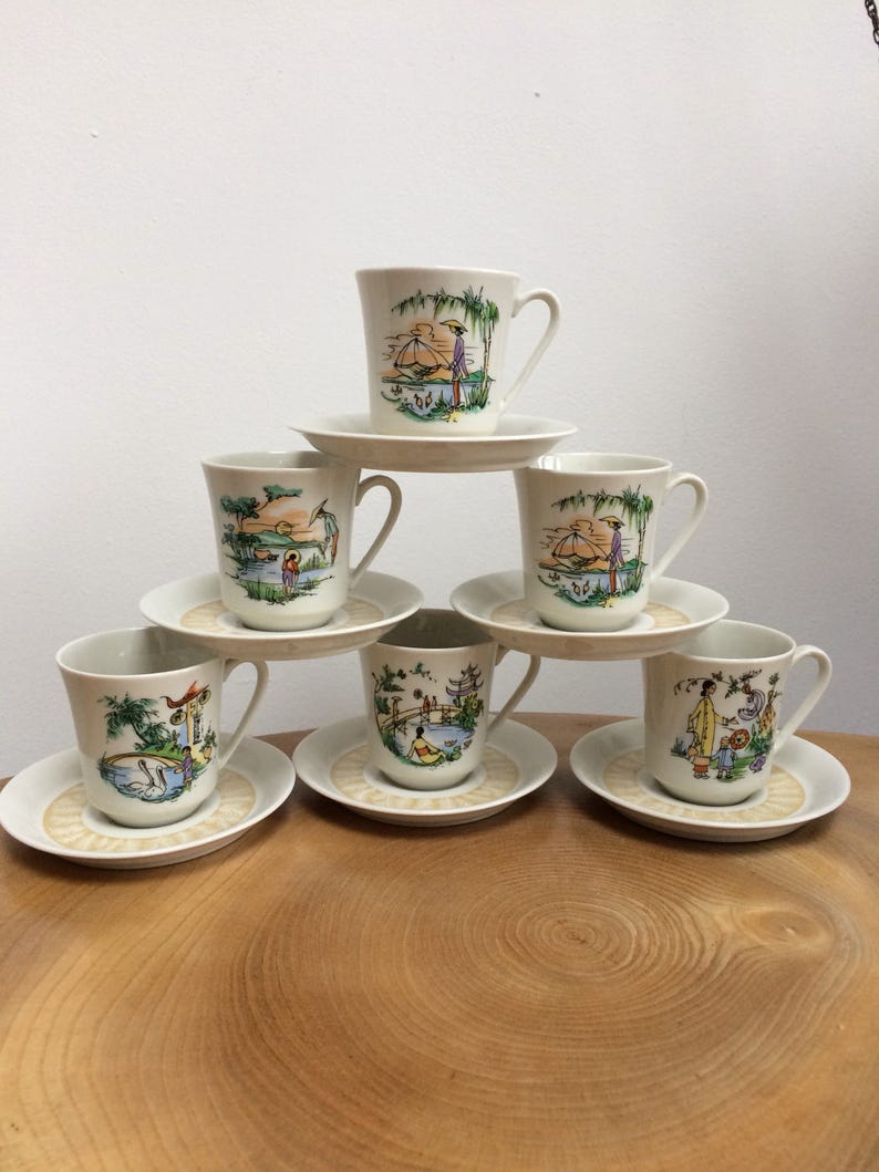 May include: Set of six white porcelain teacups and saucers with Asian-inspired designs. Each cup and saucer features a different scene with people, boats, and buildings.