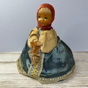 May include: A vintage doll wearing a red headscarf, a yellow and gold dress, and a blue skirt with lace trim.