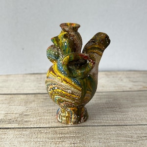 May include: A hand-painted ceramic vase with an abstract design. The vase is a mix of yellow, blue, green, and brown, with white speckles. The vase has an unusual shape with multiple openings and a curved spout. The vase is approximately 15 cm tall.