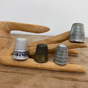 Könnte beinhalten: Vier silberne Fingerhüte, einer mit einem blau-weißen Design, auf einer Holzhand.