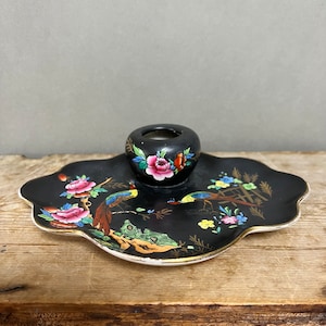 May include: A black ceramic trinket dish with a gold rim and a matching black ceramic candle holder. The dish and holder are decorated with colorful floral and bird designs.