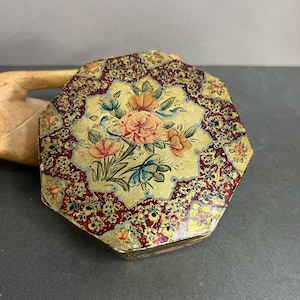 May include: An octagonal trinket box with a floral design. The box has a gold background with a red and gold floral pattern around the edges. The centre has a yellow background with pink and orange flowers.