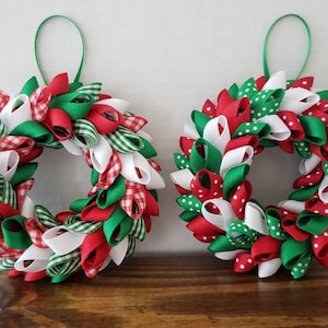 May include: Two small Christmas wreaths made of red, white, and green ribbon. One wreath has gingham ribbon and the other has polka dot ribbon.
