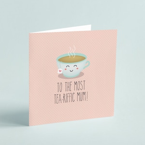 Puede incluir: Tarjeta de felicitación con fondo rosa claro y lunares blancos. Presenta una taza de té de dibujos animados sonriente con vapor y el texto "TO THE MOST TEA-RIFFIC MUM!"
