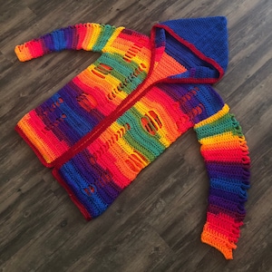 May include: A rainbow crochet cardigan with a hood. The cardigan has a distressed look with holes throughout. The hood is lined with a red fabric.