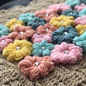 May include: A crocheted blanket with a brown background and colorful flower appliques. The flowers are made of yarn and have a rhinestone in the center. The blanket is a soft, cozy, and handmade item.