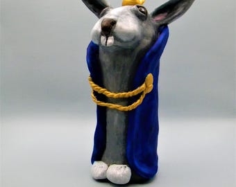 Clay rabbit sculpture clad in a royal blue robe and a crown.
