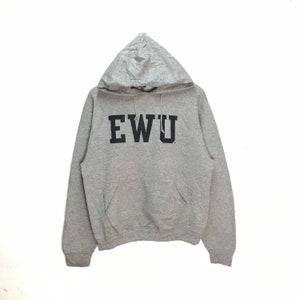 May include: A grey hooded sweatshirt featuring the black letters "EWU" across the chest. The sweatshirt has a front pocket and a drawstring hood. The material looks soft and comfortable.