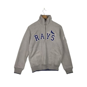 May include: A gray fleece pullover with a half-zip closure. The front of the sweatshirt features the Tampa Bay Rays logo with the team name "RAYS" in blue lettering.