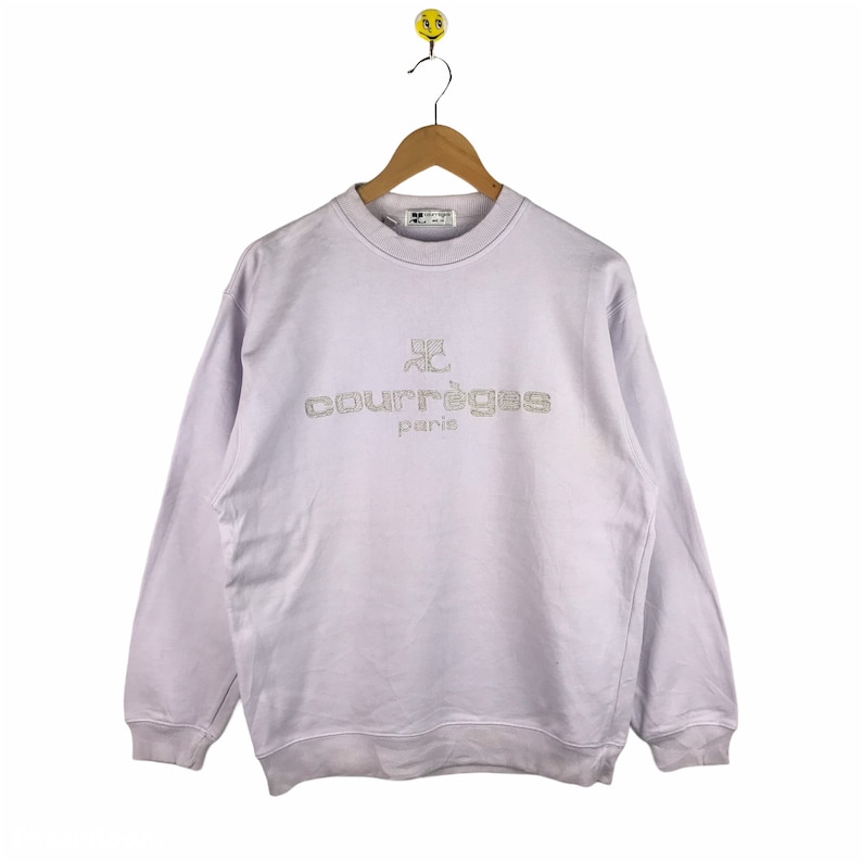 Pu&ograve; includere: Una felpa di colore lavanda con un logo ricamato bianco che dice "Courr&egrave;ges Paris".