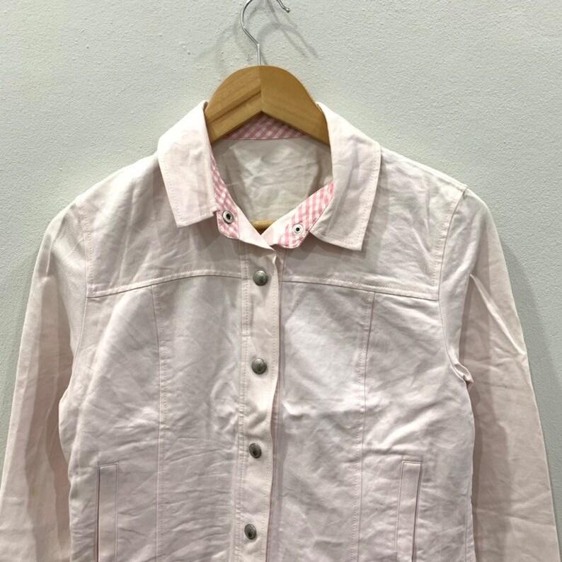 May include: A pink denim jacket with a gingham check collar. The jacket has a button front closure and long sleeves.