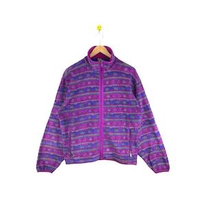 May include: A purple fleece jacket with a colourful geometric pattern. The jacket has a zip closure and two pockets.
