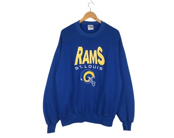 May include: A blue sweatshirt with the words "RAMS ST. LOUIS" and a Rams logo in yellow and blue.