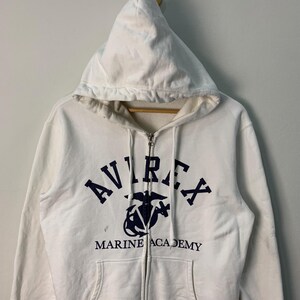 May include: A white ceramic mug with a black handle and the text "But First, Coffee" in a handwritten style. The mug is on a white surface. The mug is 4 inches tall.