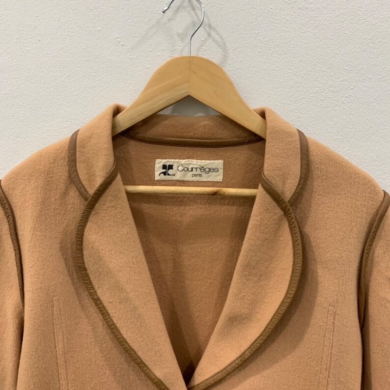 May include: A tan wool coat with brown leather trim around the collar and edges. The coat has a label that reads "Courr&egrave;ges Paris".